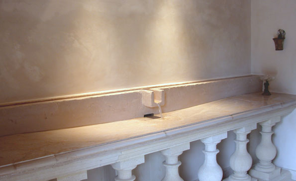 Concrete water feature/bathroom sink is cast concrete. Made to resemble an ancient carved stone bathhouse sink, hot and cold water enter from opposite sides on the top of the splashback "aqueduct". Water mixes and flows from the spout.
