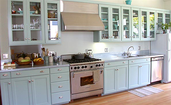 This light-filled kitchen features a full wall of custom cabinets with solid panel and glass doors, as well as a pantry custom-built to fit around an existing chimney.
